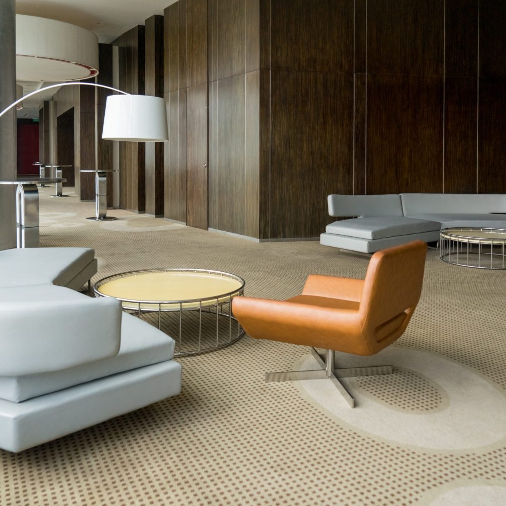 Modern hotel lobby with hallway or office lounge room. Interior with wood paneling, leather sofa and chairs, round metallic tables and floor lamp. Downtown workspace design concept